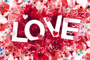 the white letters L O V E on top of red confetti wiith small pink and red  hearts
