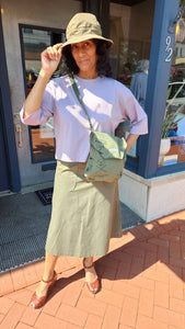 Person wearing a hat and holding a green bag on a sidewalk