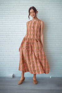 Young Woman wearing a linen dress with plaid orange and taupe and pockets in front 