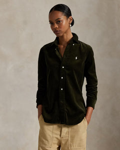 Woman wearing a dark green button-up shirt with a logo on a beige background