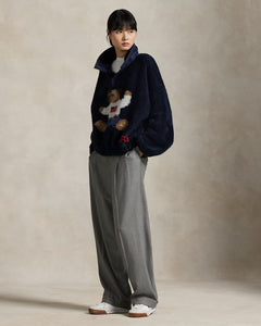 Person wearing a dark blue sweater with teddy bear design and gray pants on a beige background